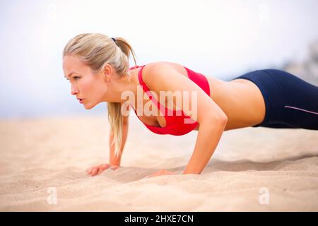 Santé du corps entier. Photo d'une jeune femme en vêtements de sport faisant des poussettes sur la plage. Banque D'Images