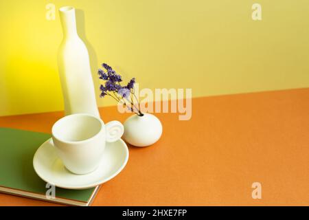 Carnet, tasse à café blanche, vase de fleur pourpre sèche sur table orange. Fond de mur jaune Banque D'Images
