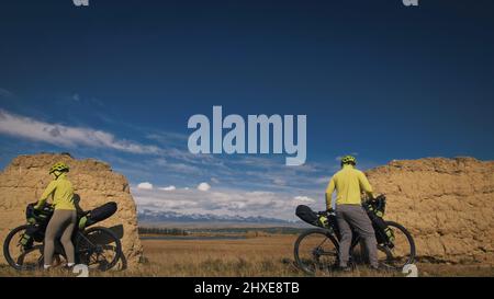 L'homme et la femme voyagent à vélo sur terrain mixte avec bikepacking. Les deux personnes voyage avec des sacs de vélo. Sport vêtements de sport dans le vert bla Banque D'Images