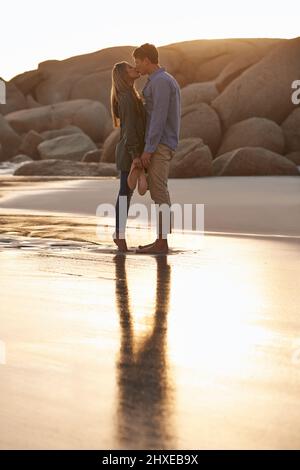 Lèvre verrouillée. Photo d'un jeune couple en train de profiter d'un baiser romantique sur la plage au coucher du soleil. Banque D'Images