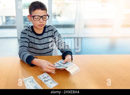 Économie pour les jours de pluie. Photo d'un jeune garçon concentré comptant son argent sur la table du dîner à la maison. Banque D'Images