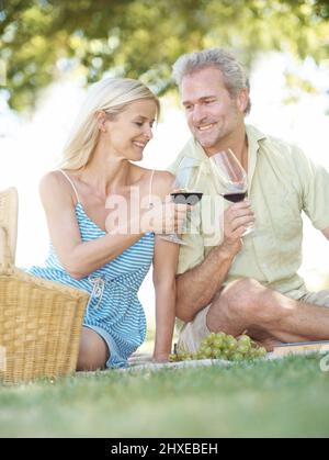 Moments romantiques dans le parc. Un mari et une femme heureux de goûter avec un verre de vin pendant qu'ils aiment pique-niquer à l'extérieur dans un parc le jour de l'été. Banque D'Images