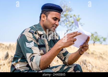 Jeune soldat indien lisant la lettre ou le courrier d'un membre de la famille pendant qu'il est au service sur le dessus de mountien - concept de famille manquante, de liaison et éloigné Banque D'Images