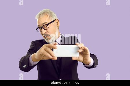 Photo studio d'un homme d'affaires expérimenté qui fait un visage amusant et prend le selfie sur son smartphone Banque D'Images