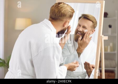 Homme souriant appliquer la crème faciale faire des procédures de beauté Banque D'Images