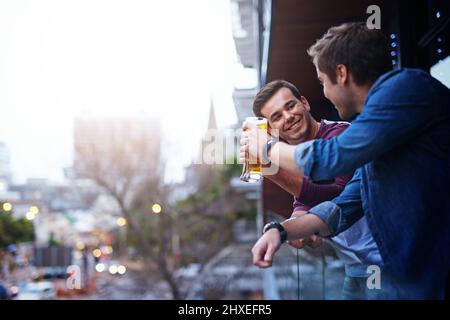 Déroulement après le travail. Coupe courte de deux gars qui boivent de la bière tout en se tenant sur le balcon lors d'une fête. Banque D'Images