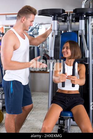 Homme bien formé coach d'aider les jeunes professionnels à l'aide de machines à l'intérieur de sport pont pec Banque D'Images