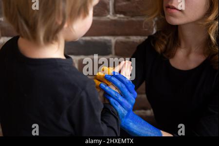 La femme calme le petit garçon, tient ses mains dans la sienne, peinte dans les couleurs jaune et bleu du drapeau ukrainien. Famille, unité, soutien. Les Ukrainiens sont contre W. Banque D'Images