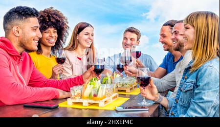 un groupe d'amis jeunes adultes qui se tient à l'extérieur avec un verre de vin dans un bar-restaurant situé sur le toit. les gens qui apprécient l'heure de l'apéritif en train de boire de l'alcool et de manger Banque D'Images