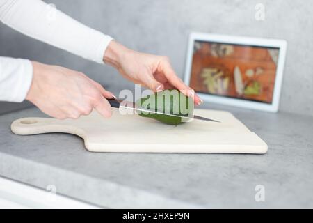 Femme mains de moitié réduire l'avocat sur la planche à découper, tutoriel de cuisine en ligne Banque D'Images