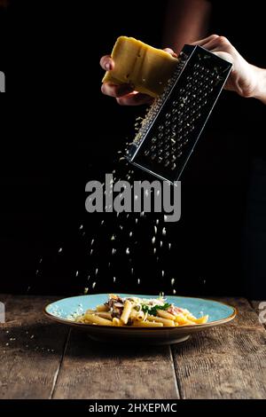 Les mains râper le fromage sur le plat de pâtes Banque D'Images