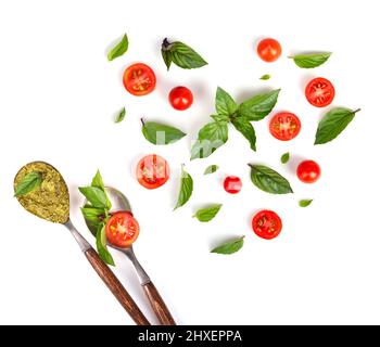 Vue de dessus des tomates, feuilles de basilic en forme de coeur et cuillères vintage avec pesto vert isolé sur fond blanc Banque D'Images