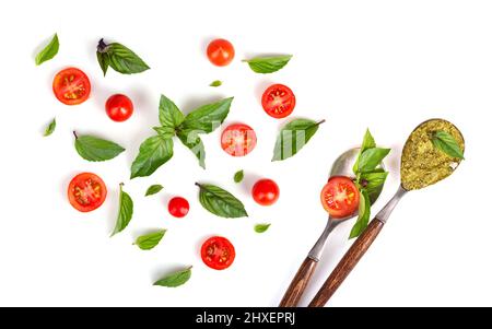 Plat de tomates, feuilles de basilic en forme de coeur et cuillères vintage avec pesto vert isolé sur fond blanc Banque D'Images