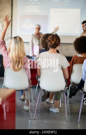 Une jeune femme qui assiste à la présentation dans une atmosphère agréable au bureau lève la main pour une question Banque D'Images