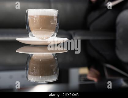 Une tasse de café cappuccino avec mousse sur une table en verre noir Banque D'Images