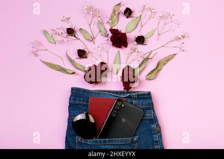 Sur fond rose, une mise en page de fleurs, passeport, téléphone portable et lunettes de soleil piquant hors de la poche des jeans Banque D'Images