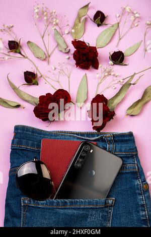 De la poche des jeans vous pouvez voir un téléphone portable, une carte d'identité et des lunettes de soleil. Fleurs sur fond rose. Banque D'Images