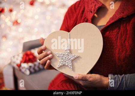 C'est un cœur pour noël. Vue rognée d'une femme tenant un cadeau de Noël en forme de coeur. Banque D'Images