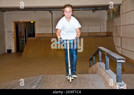 Boy est son scooter avec scooting dans un hall intérieur Banque D'Images