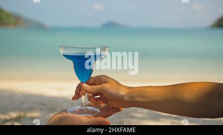 Femme prend et boit un délicieux cocktail bleu de l'homme palmier sur la plage dans l'ombre près de calme azur océan vue proche.Voyager dans les pays tropicaux Banque D'Images