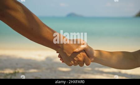 Mains de flirter jeune homme et femme touchant sur la plage dans l'ombre des palmiers contre calme azur océan vue proche. Voyager dans les pays tropicaux Banque D'Images