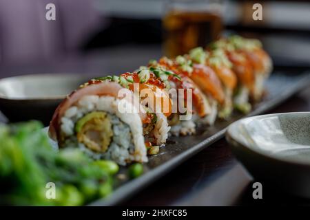 Attention sélective au Dragon Roll, un rouleau de sushis sur le dessus avec du poisson frais cru sur un plat noir. Banque D'Images