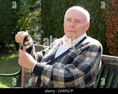 Vieil homme jouit d'assis sur un banc dans son jardin Banque D'Images