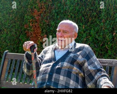 Vieil homme jouit d'assis sur un banc dans son jardin Banque D'Images