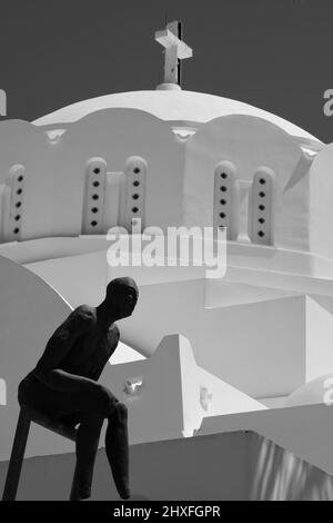 Santorini, Grèce - 10 mai 2021 - une statue abstraite et une église orthodoxe grecque blanchie à la chaux en arrière-plan à Santorini, en noir et blanc Banque D'Images