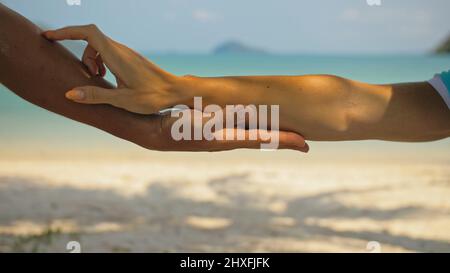 Mains de flirter jeune homme et femme touchant sur la plage dans l'ombre des palmiers contre calme azur océan vue proche. Voyager dans les pays tropicaux Banque D'Images