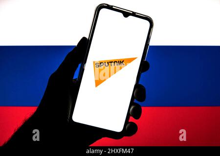 Sur cette photo, un logo Spoutnik apparaît sur un smartphone avec un drapeau de la Russie en arrière-plan. Banque D'Images