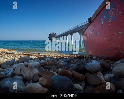 Une vue à angle bas de l'ombre d'un bateau abandonné sur la rive à Bembridge, y compris un grand ciel bleu et la mer, et la station de canot de sauvetage locale. Banque D'Images