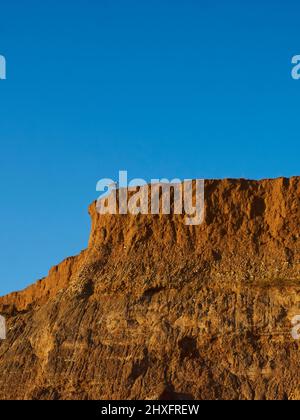 Une vue quelque peu abstraite des falaises de la baie de Compton, avec le soleil d'automne qui fait briller les riches couleurs chaudes des rochers contre le ciel bleu. Banque D'Images