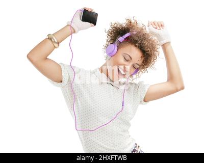 La vie est une chanson. Chantez avec lui. Studio tourné d'une jeune femme attrayante écoutant de la musique sur son téléphone sur fond blanc. Banque D'Images