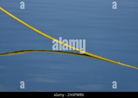 Bateau à voile nylon jaune double tresse corde d'amarrage sur la surface bleue de l'eau de mer. Banque D'Images