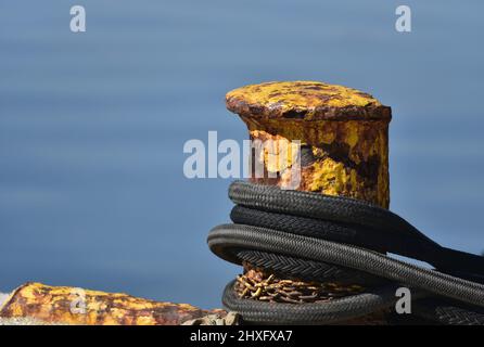 Corde d'amarrage double tressée en nylon nautique sur un bollard jaune rouillé contre la mer bleue. Banque D'Images