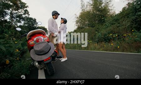 J'adore un couple sur une moto rouge vêque de vêtements blancs pour faire un voyage sur la route de la forêt. Deux touristes caucasiens, homme, conduisent en scooter. Location de moto, coffre-fort Banque D'Images