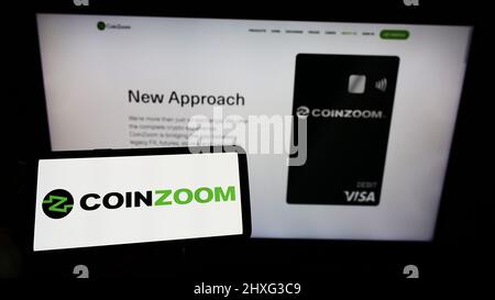 Personne tenant un smartphone avec le logo de la société américaine d'échange de crypto CoinZoom Inc. À l'écran devant le site Web. Mise au point sur l'affichage du téléphone. Banque D'Images