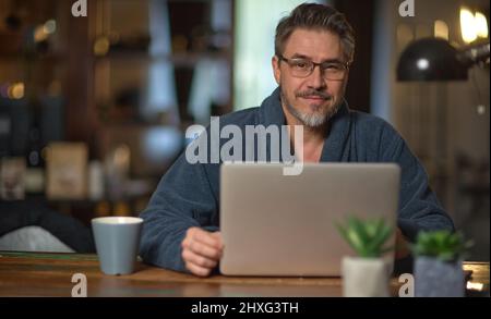 Homme d'affaires à la maison, au bureau, portant un peignoir et un ordinateur portable Banque D'Images