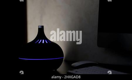 Diffuseur d'huile d'aromathérapie avec lumière LED colorée à partir de laquelle la vapeur s'échappe sur un fond sombre. Concept. Humidificateur aromatique sur une table à la maison. Banque D'Images