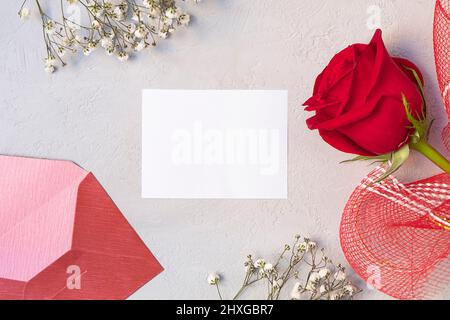 Composition florale avec rose rouge, fleurs blanches, enveloppe et carte en papier vierge. Vue de dessus, plan d'appartement Banque D'Images