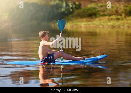 L'été, il suffit de suivre le flux. Photo d'un adolescent qui aviron son kayak sur un lac. Banque D'Images