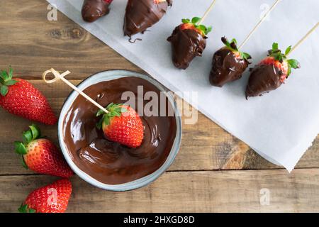 Fraises au chocolat sur fond de bois. Processus de trempage des fraises dans le chocolat. Copier l'espace. Banque D'Images