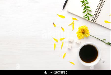 Tasse blanche de bloc-notes et stylo sur une table blanche. Autour des pétales des fleurs et des feuilles flétrissent. Vue de dessus. Composition plate. Bac léger Banque D'Images