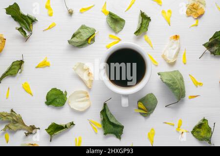 Une tasse de café blanc sur une table blanche. Autour des pétales des fleurs et des feuilles flétrissent. Vue de dessus. Composition plate. Arrière-plan clair. Banque D'Images