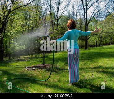 femme en pyjama arroser jeune arbre rouge Banque D'Images