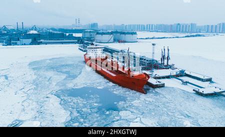 Terminal de pétrole du Nord dans la neige et le tanker illuminé par des lumières rouges amarrées sur l'eau de l'océan couvert de morceaux de glace à la vue aérienne du crépuscule soir Banque D'Images