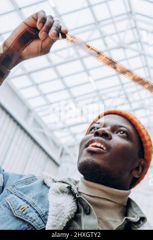 Le photographe afro-américain passionné en veste denim regarde un film vintage dans une pièce très éclairée Banque D'Images