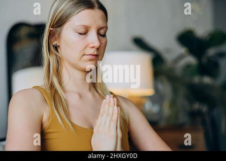 Femme sportive avec cheveux blonds et tatouages en haut et jambières médite avec grand sourire assis dans la pose de lotus sur le tapis de yoga vue rapprochée Banque D'Images