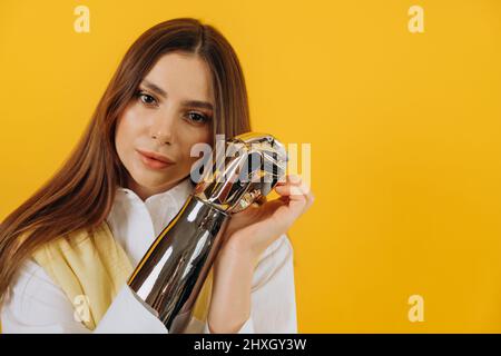 Jeune femme blonde aux cheveux longs en chemise blanche et veste montre le bras bionique contemporain debout sur fond jaune vif Banque D'Images